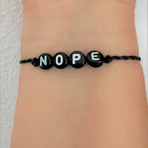 May include: Black string bracelet with black beads that spell out the word "NOPE" in white letters.