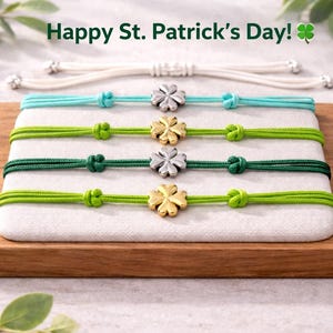 May include: A collection of St. Patrick's Day themed bracelets. The bracelets are displayed on a wooden tray and feature green, blue, and white cords with clover charms. The text "Happy St. Patrick's Day!" is visible at the top.