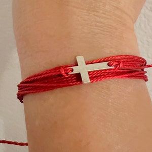May include: Red string bracelet with a silver cross charm.