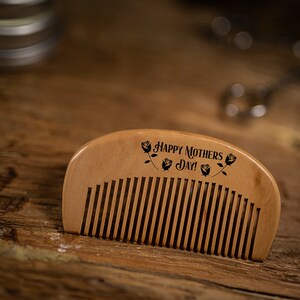 May include: A wooden comb with a rounded handle and the text "Happy Mothers Day!" engraved on the top. The comb has a natural wood finish and is decorated with small rose designs.