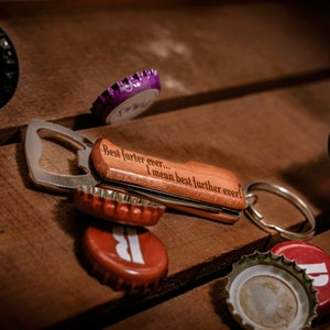 May include: A wooden bottle opener keychain with a metal bottle opener and a key ring. The keychain has the inscription "Best farter ever... I mean best farther ever!"