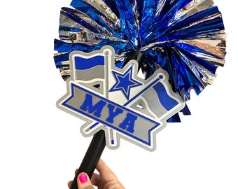 May include: A cheerleading pom-pom attached to a black handle featuring a decorative plaque. The plaque displays the name MYA in blue letters on a grey banner, flanked by two flags with blue and grey stripes and a central blue star emblem.