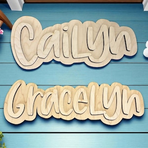 May include: Two wooden name signs, "Cailyn" and "Gracelyn", in a cloud-shaped design. The names are layered for a 3D effect. The signs are made of light-colored wood and are displayed on a blue background.
