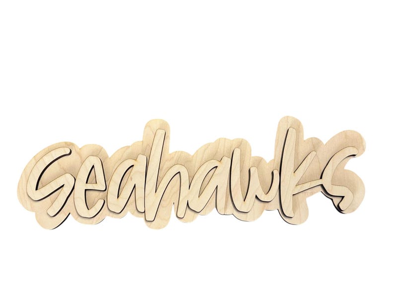 May include: Wooden sign with the word "Seahawks" in a cursive font. The sign is made of light-colored wood with a dark outline, and the letters are layered for a 3D effect. The sign is a decorative item.