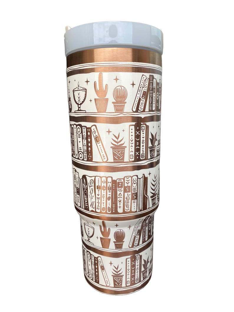 May include: A white and copper tumbler with a bookshelf design. The tumbler features a pattern of books, plants, and stars in a copper color on a white background.