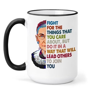 May include: White ceramic mug with a black handle and black rim. The mug features a colorful illustration of Ruth Bader Ginsburg and a quote: "Fight for the things that you care about, but do it in a way that will lead others to join you."