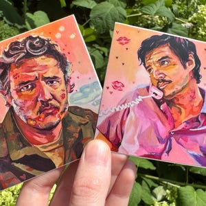 May include: Two square art prints depicting portraits of a man. One shows him with a serious expression, the other on the phone. Both have a pink background with red kiss marks. The art style is painterly.