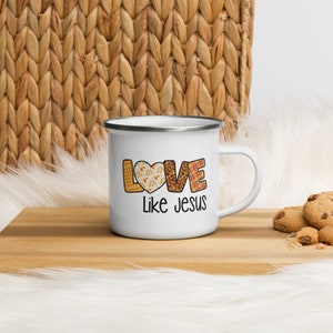 May include: White enamel mug with a silver rim and handle. The mug features a patchwork design of the word "LOVE" with a heart in the "O". The text "Like Jesus" is printed below the word "LOVE".