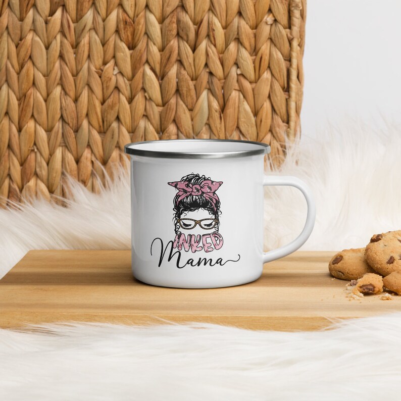 May include: White enamel mug with a black and white illustration of a woman with a pink bow in her hair and the text "INKED MAMA" in pink letters.