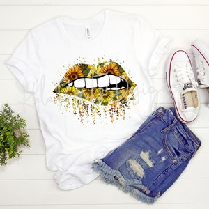 May include: White t-shirt with a graphic of a pair of lips covered in sunflowers. The lips are slightly open, showing teeth. The background is a white wood surface.