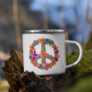 May include: White enamel mug with a peace sign made of colorful flowers. The peace sign is surrounded by a ring of flowers in shades of orange, yellow, red, purple, and green.