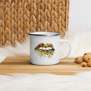 May include: White enamel mug with a black outline. The mug features a graphic of a pair of lips with a sunflower pattern.