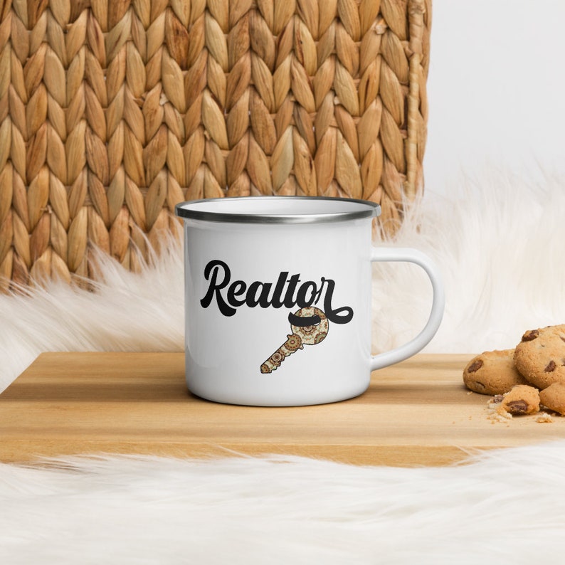 May include: White enamel mug with a black and white illustration of a key with a moustache and the word "Realtor" in black script.