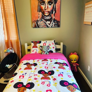 May include: A white and pink twin-sized bed with a white comforter featuring a repeating pattern of black girls with afro puffs and rainbows. The comforter has a pink and white pillow with a black girl with afro puffs and a gray elephant plush toy. The bed is in a room with a painting of a woman with a colorful head wrap and a calendar on the wall.