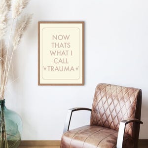 Peut inclure: Une impression encadrée beige avec le texte "NOW THATS WHAT I CALL *TRAUMA*" en texte brun.
