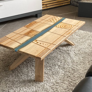 Peut inclure: Une table basse en bois avec une rivière en époxy bleue traversant le centre. Le plateau de la table est composé de plusieurs morceaux de bois, créant un motif unique.