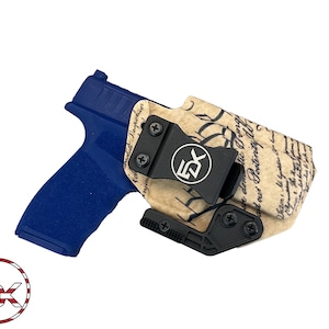 May include: A blue and black gun holster with a brown and black printed design featuring the text of the Declaration of Independence. The holster has a black clip and a black adjustable retention device.