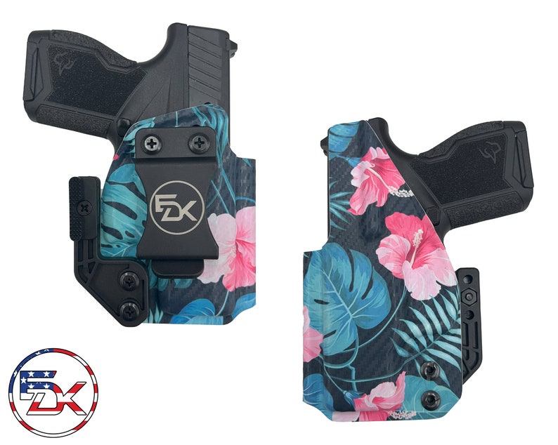Puede incluir: Una funda de pistola negra con estampado floral tropical con flores de hibisco rosas y hojas de palmera azules. La funda tiene un clip negro y una placa de metal negra con las letras "FDX" en ella.