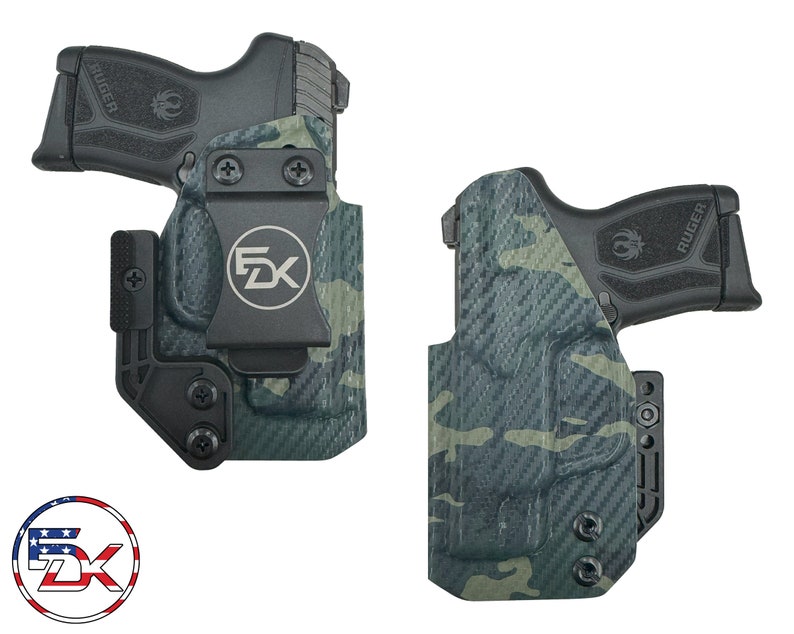 May include: A black and green camouflage concealed carry holster with a black belt clip and a black polymer pistol with the word "RUGER" printed on the side.