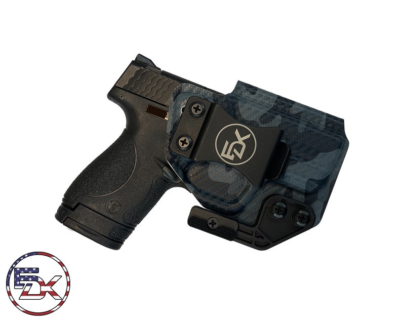 May include: Black handgun with a black and blue camouflage holster. The holster has a black clip with the letters "5X" on it. The image is on a white background.