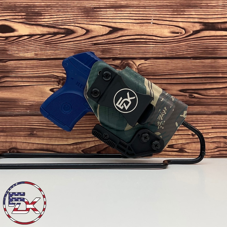 May include: A blue and black handgun holster with a camouflage pattern. The holster is made of durable material and features a secure clip for easy carrying.