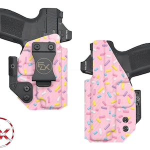 May include: Two pink and white patterned holsters for concealed carry of a handgun. The holsters have a black clip and a black trigger guard. The pattern is reminiscent of sprinkles on a pink cake.