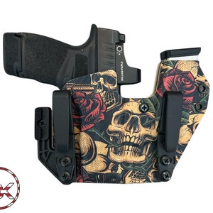 May include: A black handgun holster with a skull and roses design. The holster has a clip on the side and is made of a durable material.