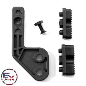 May include: A set of black metal mounting components, comprising an L-shaped bracket, two rectangular pieces with textured sides, and a bolt. The items are displayed against a white backdrop.