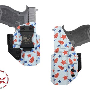 May include: A white, blue, and red patterned gun holster with a black clip. The pattern features red and blue popsicles and white stars on a white background. The holster is designed to fit a handgun.