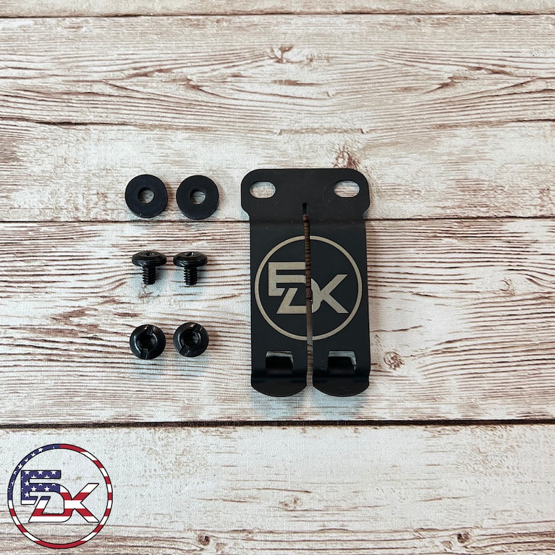 May include: A black metal clip with the letters "EZK" in a silver circle, along with two screws, two washers, and two small black fasteners. The clip has two slots and two holes. The EZK logo is in the center.