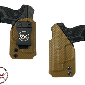 May include: A tan leather holster with a black clip and a black Ruger pistol inside. The holster has a carbon fiber pattern and the clip has the letters "FDX" printed on it.