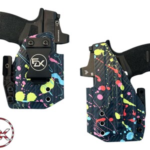 May include: Two black holsters with a carbon fiber texture and a neon paint splatter pattern in pink, yellow, and blue. Each holster contains a black handgun with a mounted optic sight. A circular logo with the letters FDK and a flag design is visible.