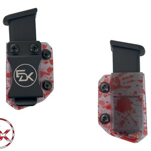 May include: Two black magazine carriers with a red and white splatter pattern. The carriers have a black clip and a metal plate with the letters "FDX" on them.