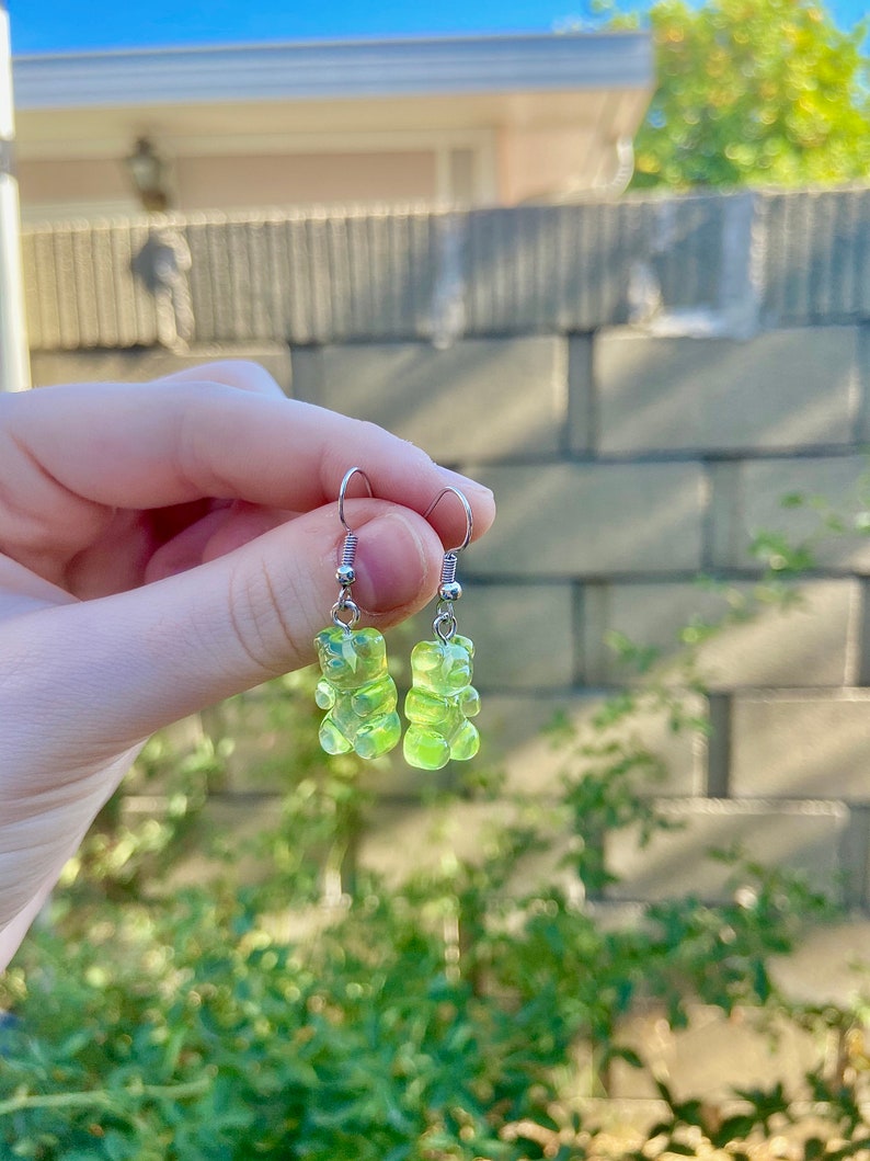 K&ouml;nnte beinhalten: Ein Paar silberne Ohrringe mit gr&uuml;nen Gummib&auml;rchen-Anh&auml;ngern.