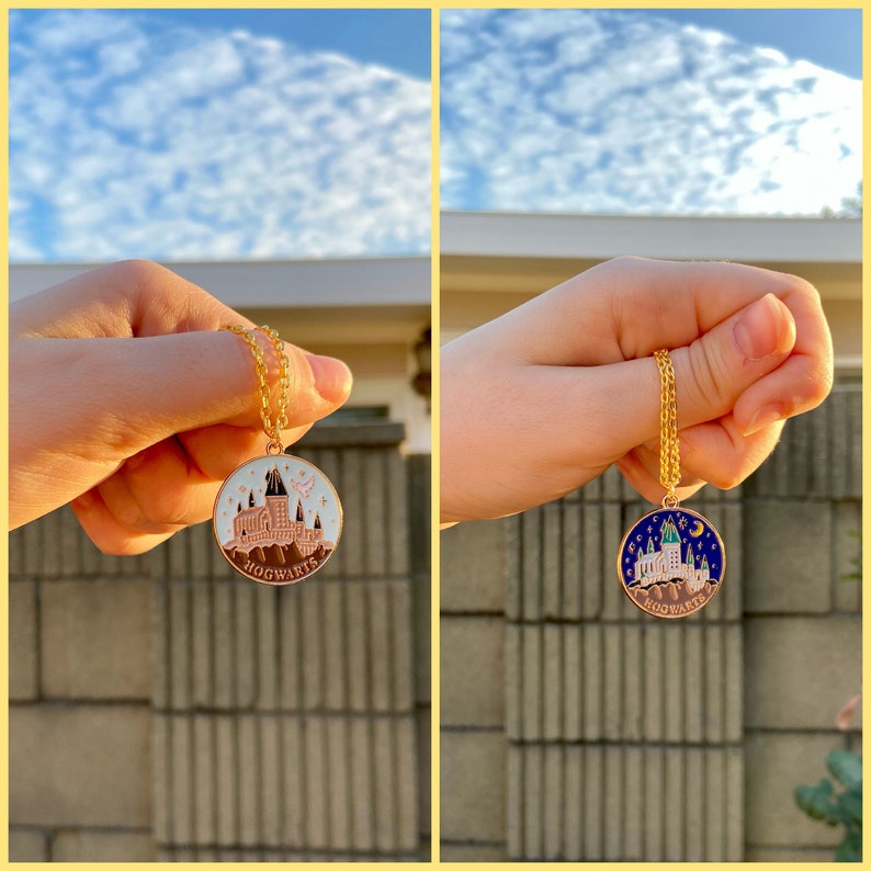 May include: Two gold necklaces with round pendants featuring a detailed illustration of Hogwarts castle. One pendant has a white background with pink accents, the other has a blue background with green accents. Both pendants say "Hogwarts" at the bottom.