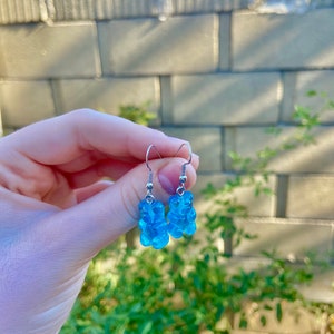 K&ouml;nnte beinhalten: Ein Paar blaue Gummib&auml;rchen-Ohrringe mit silbernen Haken.