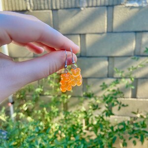 K&ouml;nnte beinhalten: Ein Paar silberne Ohrringe mit orangefarbenen Gummib&auml;rchen-Anh&auml;ngern.