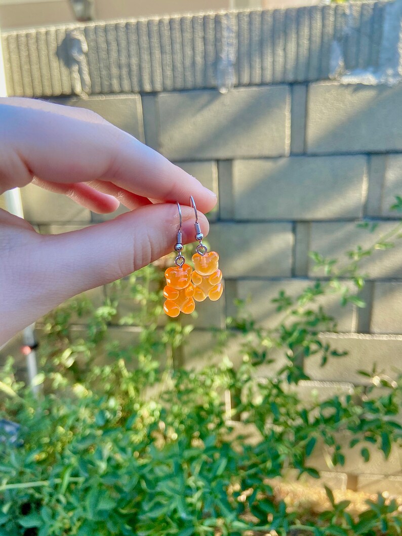 K&ouml;nnte beinhalten: Ein Paar silberne Ohrringe mit orangefarbenen Gummib&auml;rchen-Anh&auml;ngern.