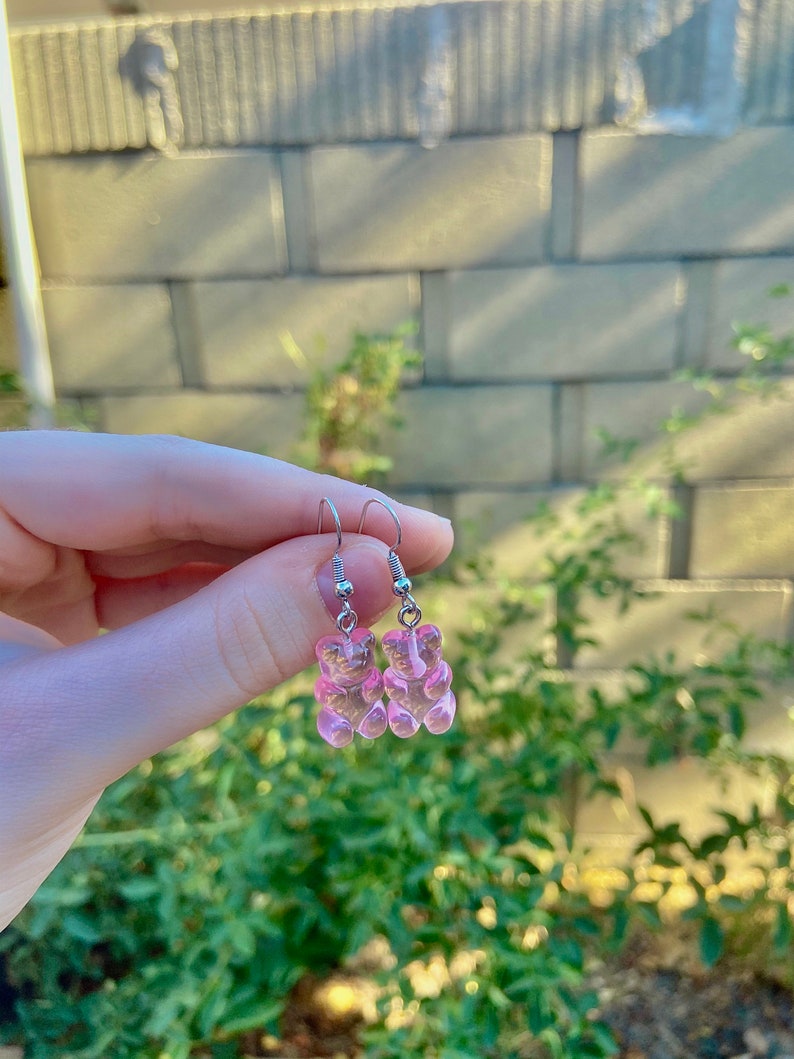 K&ouml;nnte beinhalten: Ein Paar silberne Ohrringe mit rosa Gummib&auml;rchen-Anh&auml;ngern.
