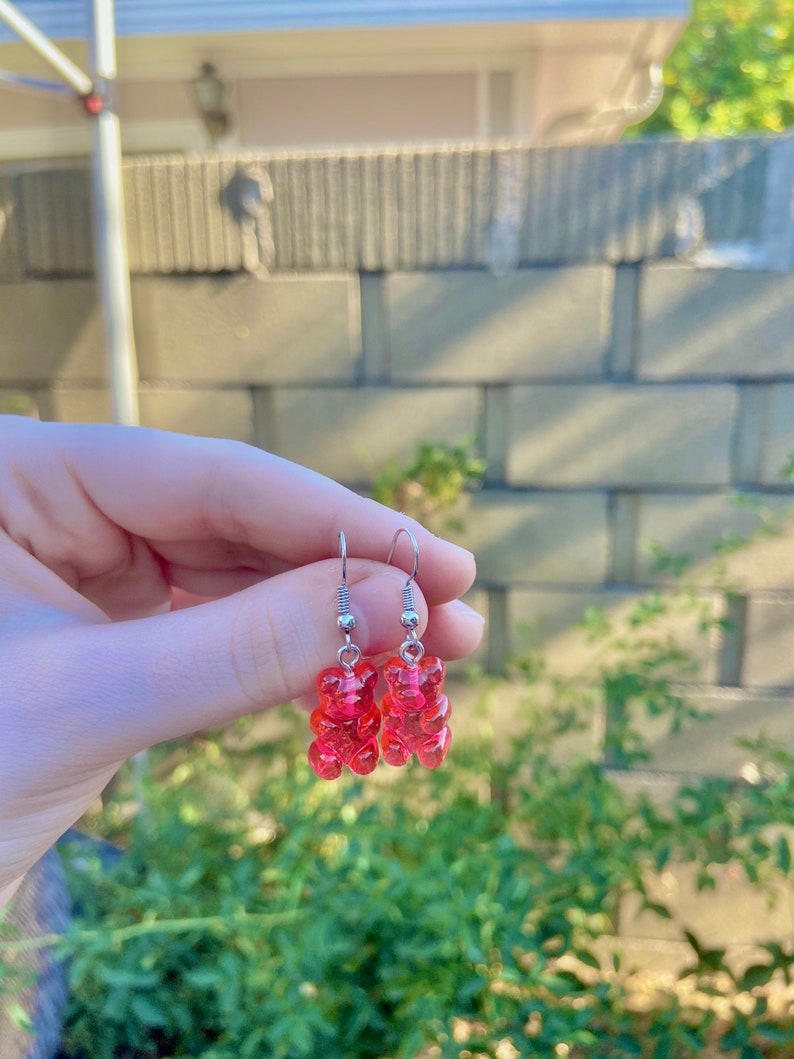 K&ouml;nnte beinhalten: Ein Paar silberne Ohrh&auml;nger mit rosa Gummib&auml;rchen-Anh&auml;ngern.