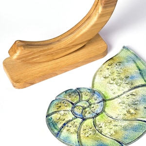 May include: A wooden stand with a curved top holds a glass nautilus shell with a blue and green mosaic design. The shell has a textured surface with small bubbles.