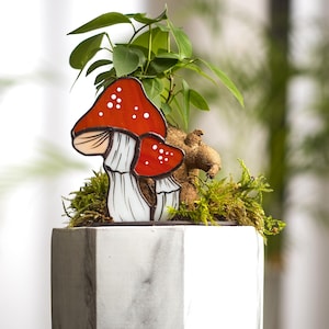 May include: A stained glass mushroom decoration with red and white accents. The mushroom is sitting on top of a potted plant with green moss.