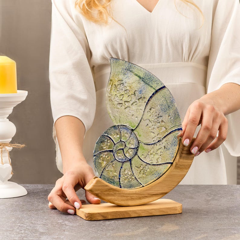 May include: A decorative glass nautilus shell sculpture with a blue and green swirl pattern, mounted on a wooden base.