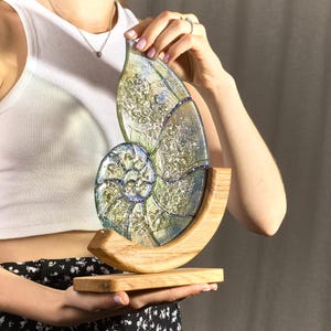 May include: A glass sculpture of a nautilus shell with iridescent green and blue colors. The shell is mounted on a wooden base.