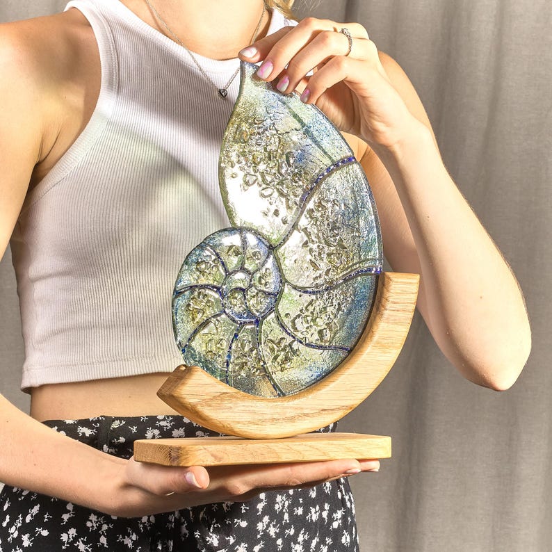 May include: A glass nautilus shell sculpture with a blue and green iridescent finish, mounted on a wooden base.