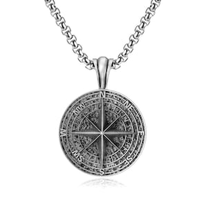 May include: A silver-colored compass pendant necklace. The pendant features a detailed compass rose design with directional markings (N, NE, E, SE, S, SW, W, NW) and a textured background. The chain is a rounded box link style.