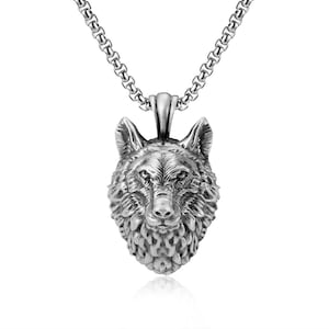 Può includere: Una collana con pendente color argento con un pendente a forma di testa di lupo dettagliata. Il volto del lupo è scolpito in modo intricato, mostrando la consistenza della pelliccia e i lineamenti del viso. La catena è a maglie e il pendente è appeso a un piccolo anello.
