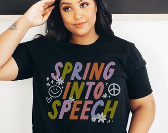 May include: A black t-shirt with the text "Spring into Speech" in colorful letters. The text is surrounded by small flowers, a peace sign, and a smiley face.
