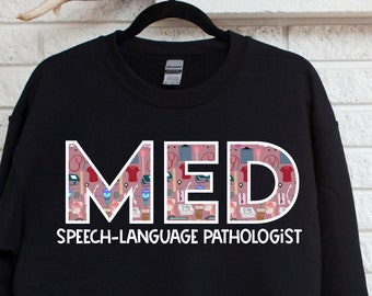 May include: Black sweatshirt with the word "MED" in white outlined letters. The letters are filled with a pattern of pink and white speech therapy related icons. Below the word "MED" is the text "SPEECH-LANGUAGE PATHOLOGIST" in white.