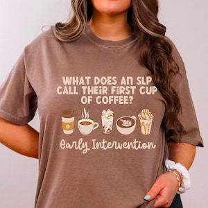 Puede incluir: Una camiseta marrón con el texto "WHAT DOES AN SLP CALL THEIR FIRST CUP OF COFFEE?" y "Early Intervention". La camiseta presenta ilustraciones de diferentes bebidas de café, incluyendo una taza para llevar, una taza humeante y un latte.